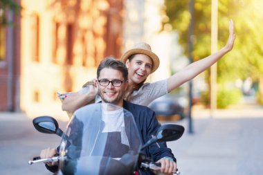 Mutlu, olgun bir çift güneşli bir günde şehirde scooter kullanıyor.