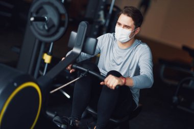Yetişkin bir adam spor salonunda maske takıyor.