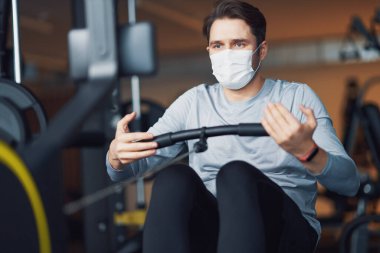 Yetişkin bir adam spor salonunda maske takıyor.