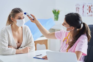 Maskeli doktor, kadın hastasına teşhisi açıklıyor.