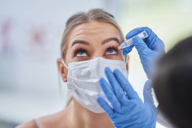 Maskeli göz doktoru kadın hastayı kontrol ediyor.