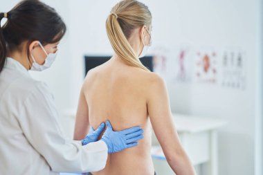 Maskeli doktor hastasının göğüslerini kontrol ediyor.