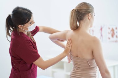 Maskeli fizyoterapist kadın hastaya yardım ediyor.