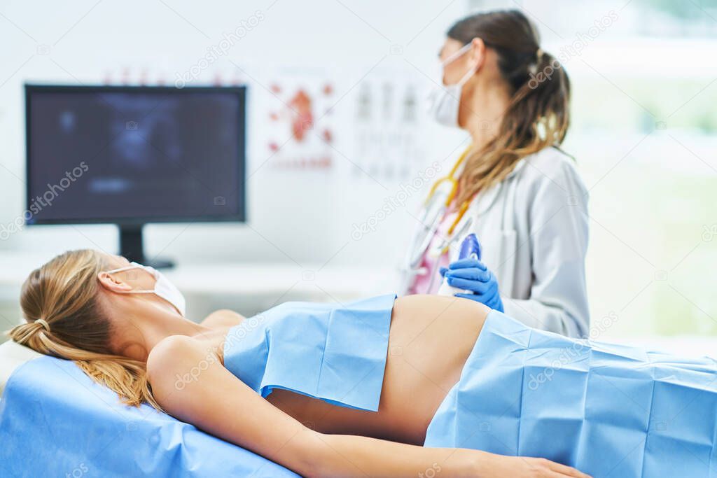 Doctor in mask doing ultrasound to her pregnant patient