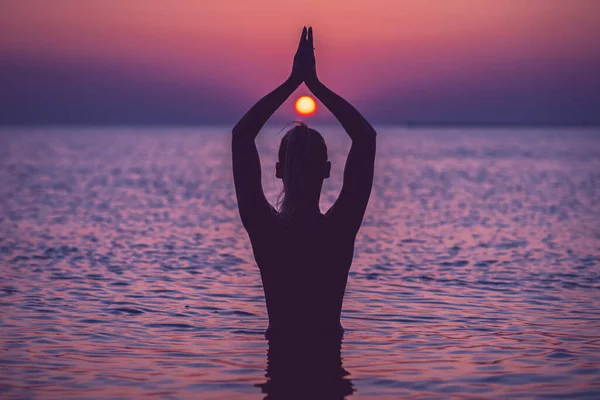 Silhueta de jovem praticando ioga na praia ao nascer do sol — Fotografia de Stock