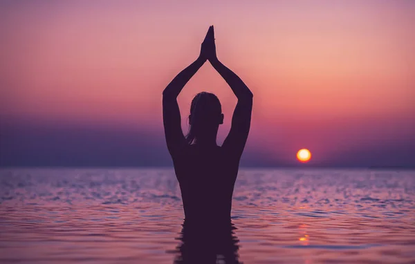 Silueta mladé ženy cvičící jógu na pláži při východu slunce — Stock fotografie