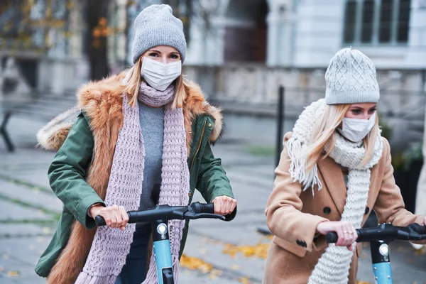 Chicas amigas con máscaras faciales y desplazamientos en scooter en la ciudad —  Fotos de Stock