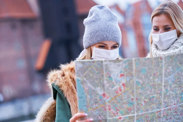 Dos mujeres usando máscaras y sosteniendo el mapa mientras visitan Gdank en Polonia —  Fotos de Stock