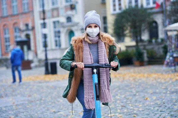 Mujer con máscara facial y desplazamientos en scooter en la ciudad —  Fotos de Stock