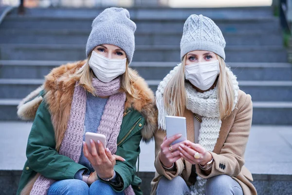 Två kvinnor använder smartphones och bär masker i staden — Stockfoto