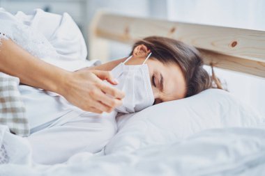 Maskeli yetişkin kadın evde kendini hasta hissediyor. Covid-19 konsepti.