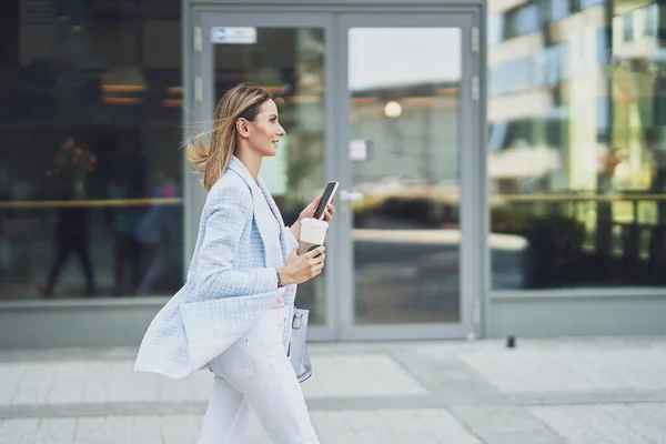 Volwassen aantrekkelijke vrouw met smartphone wandelen in de stad — Stockfoto