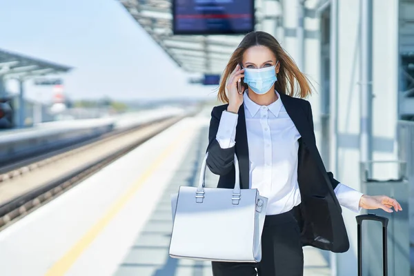 Elegant woman in mask walking with bag and suitcase in the railway station — Stock Photo, Image