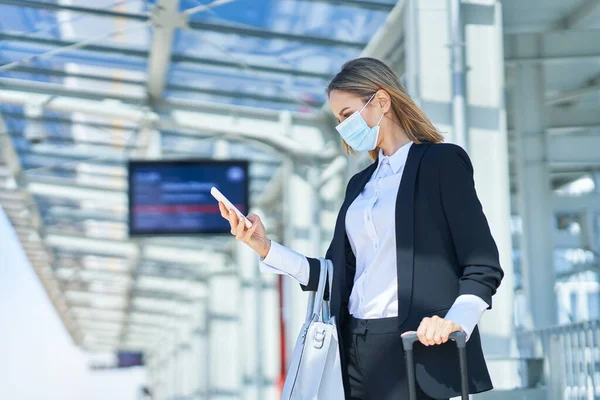 Elegant kvinna i mask går med väska och resväska på järnvägsstationen — Stockfoto