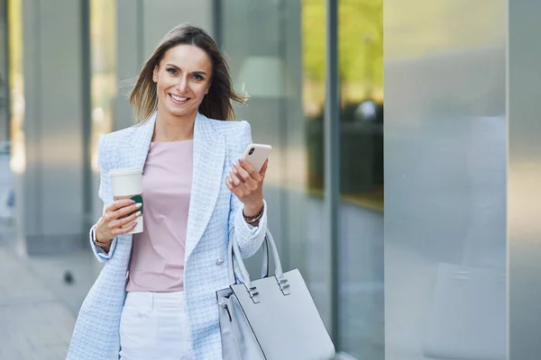 Mujer atractiva para adultos con smartphone caminando en la ciudad —  Fotos de Stock