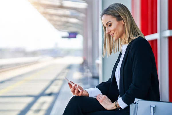 Elegant kvinna sitter och väntar på tåget på järnvägsstationen — Stockfoto