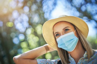 Maskeli kadın parkta şapka takıyor..