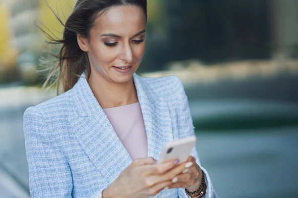 Volwassen aantrekkelijke zakenvrouw met smartphone wandelen in de stad — Stockfoto