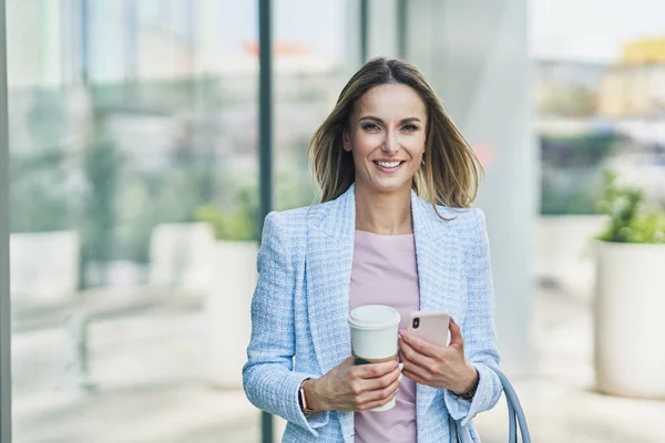Adult attractive Business woman with smartphone and coffee walking in the city