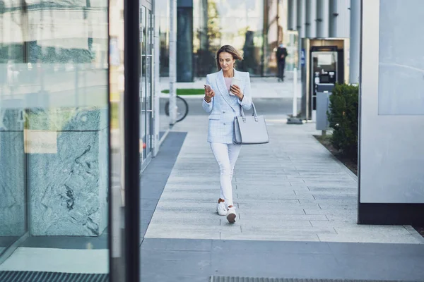 Volwassen aantrekkelijke vrouw met smartphone wandelen in de stad — Stockfoto