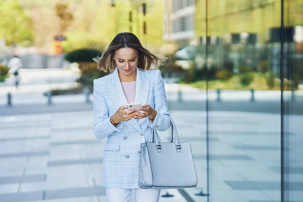Volwassen aantrekkelijke zakenvrouw met smartphone wandelen in de stad — Stockfoto