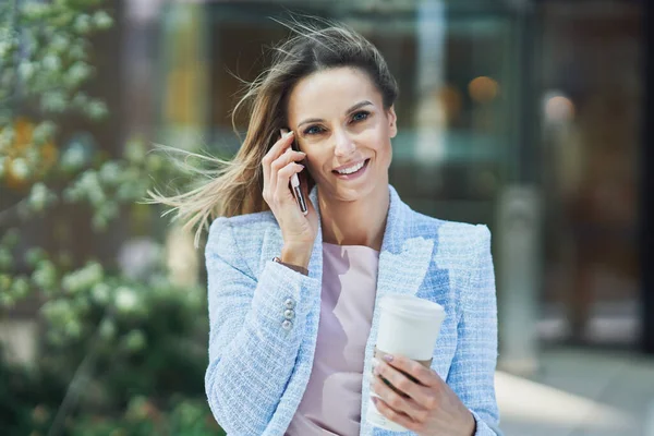 Yetişkin çekici iş kadını akıllı telefon ve kahve ile şehirde yürüyor. — Stok fotoğraf