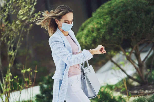 Donna attraente adulta in maschera con smartphone che cammina in città — Foto Stock