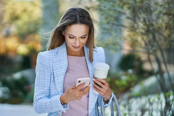 Volwassen aantrekkelijke zakenvrouw met smartphone en koffie wandelen in de stad — Stockfoto