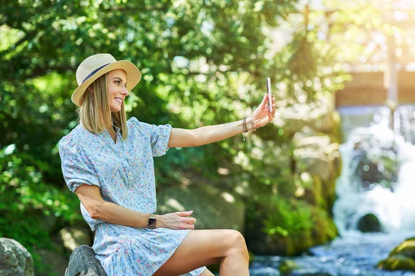 Een leuk meisje zittend op een rots met smartphone — Stockfoto