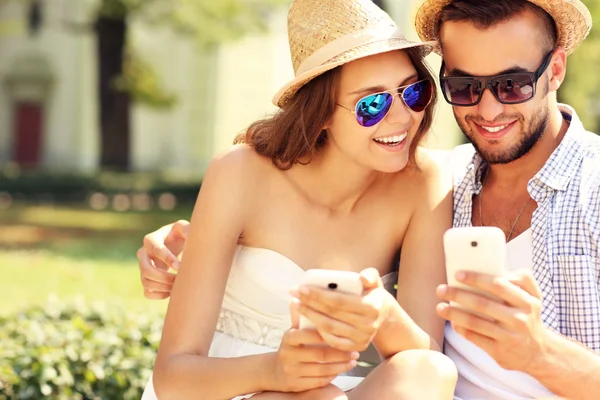 Casal alegre usando smartphones no parque — Fotografia de Stock