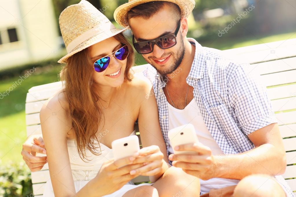 Young couple sitting on a bench with smartphones