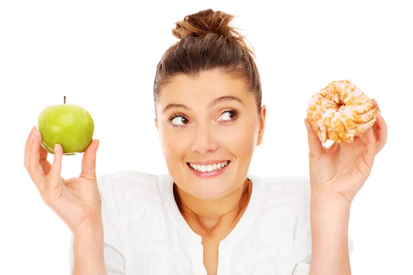 Женщина выбирает между яблоком и пончиком Стоковое Фото