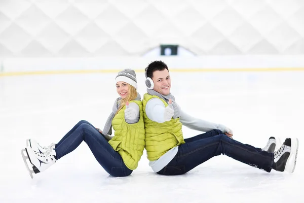 Couple joyeux assis sur la patinoire — Photo