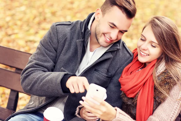 Jeune couple sur un banc avec smartphone dans le parc — Photo