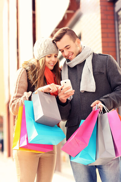 Happy couple shopping in the city with smartphone