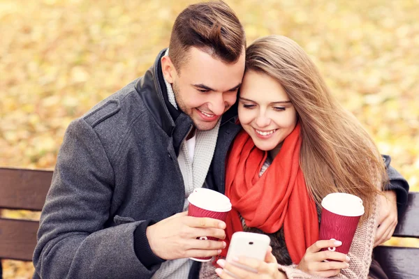 Jeune couple sur un banc avec smartphone dans le parc — Photo