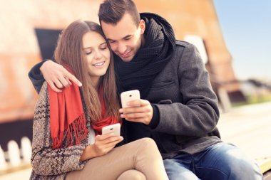 Çift bir bankta oturan ve akıllı telefonlar kullanma