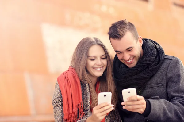 Couple sitting on a bench and using smartphones — Stock Photo, Image