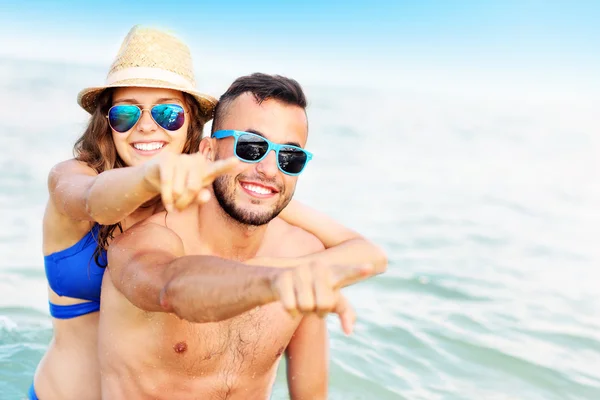 Gelukkige paar wijzend op het strand — Stockfoto