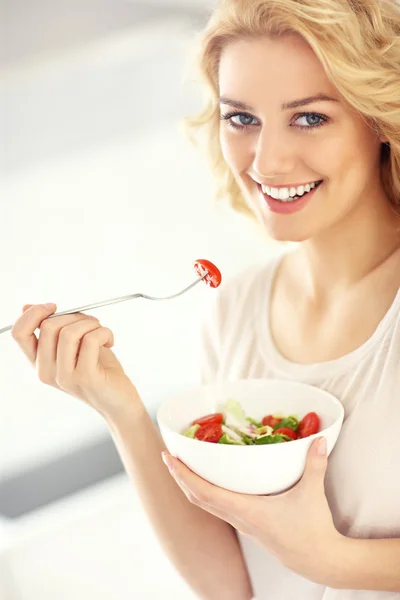 Jovem mulher comendo salada na cozinha — Fotografia de Stock