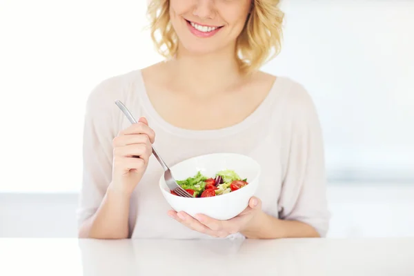 Giovane donna che mangia insalata in cucina — Foto Stock