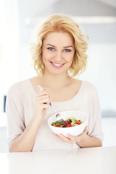Jonge vrouw eet salade in de keuken — Stockfoto