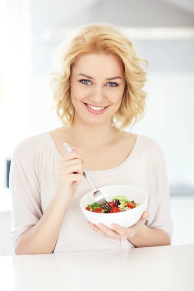 Jovem mulher comendo salada na cozinha — Fotografia de Stock