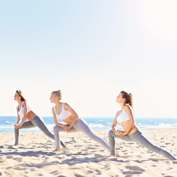 Grupp kvinnor som utövar yoga på stranden — Stockfoto