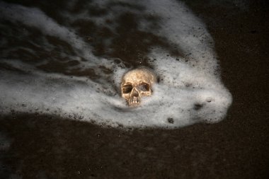 İNSAN SKULL. İnsan Kafatası sahile vuruyor. İnsan Kafatası kuma gömüldü. Kumda insan kafatası dalgalar ve deniz köpüğüyle okyanus..