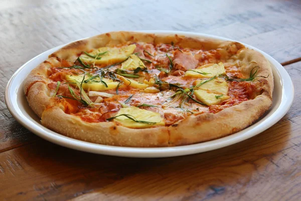 Hawaiian Pizza. A Ham and Pineapple Pizza on a white plate on a wooden table for lunch. Pizza is enjoyed world wide by hungry people. Pizza Pizza Everywhere.