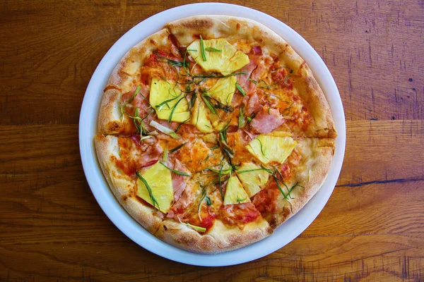 Hawaiian Pizza. A Ham and Pineapple Pizza on a white plate on a wooden table for lunch. Pizza is enjoyed world wide by hungry people. Pizza Pizza Everywhere.