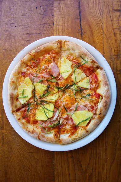 Hawaiian Pizza. A Ham and Pineapple Pizza on a white plate on a wooden table for lunch. Pizza is enjoyed world wide by hungry people. Pizza Pizza Everywhere.