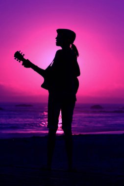 Tanımlanamayan genç bir kadın Laguna Beach California 'da güneş batarken gitarını çalıyor. Akustik gitarlı bir kız. Herkes için müzik çalmak. Gün batımında müzik çalan ve şarkı söyleyen bir kızla. Kaliforniya Günbatımı. 