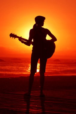 Tanımlanamayan genç bir kadın Laguna Beach California 'da güneş batarken gitarını çalıyor. Akustik gitarlı bir kız. Herkes için müzik çalmak. Gün batımında müzik çalan ve şarkı söyleyen bir kızla. Kaliforniya Günbatımı. 